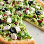 Chicken Crust Caesar Salad Pizza topped with fresh lettuce, avocado slices, black olives, and pomegranate seeds.